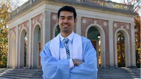 Pramit posing in front of bell tower with Carolina Blue ceremonial robes.